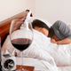 Hungover woman lies in bed glaring at glass of wine